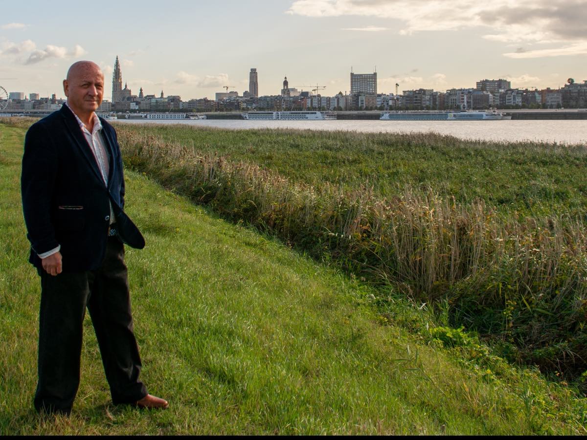 Marc Dassen wandelend op de dijk langs de Schelde tegenover Antwerpen.