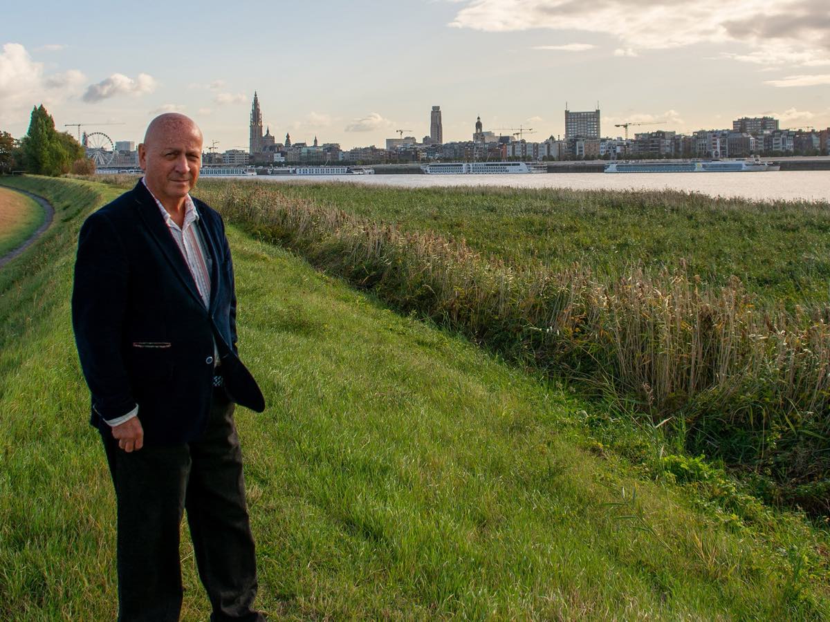 Marc Dassen op het dijkpad langs de Schelde, met de rivier en de stad op de achtergrond.